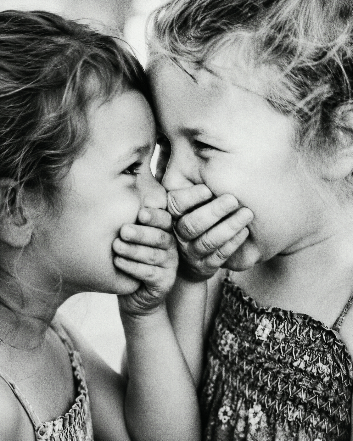 Two young girls laughing, hands over each other’s mouths